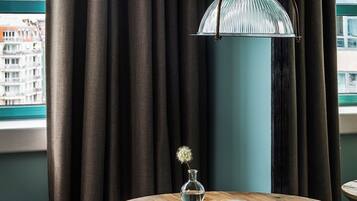 Una habitación de hotel con una mesa redonda de madera, un libro abierto, un jarrón con una flor y una lámpara colgante.