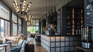 Zona de bar moderna con una barra larga, asientos y un amplio ventanal que proporciona luz natural.