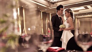 Una pareja vestida de novios en un elegante comedor con mesas dispuestas para una comida.