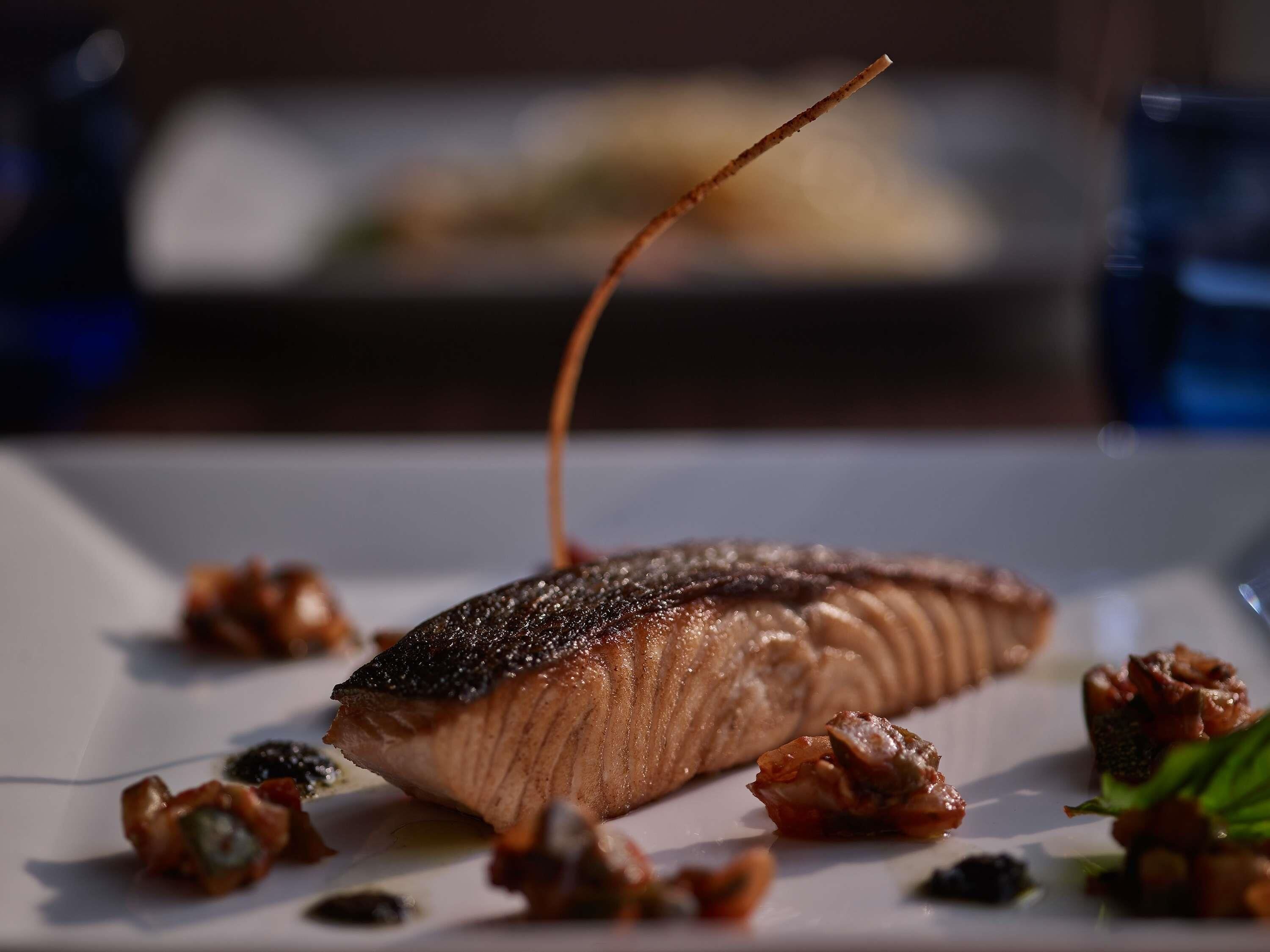 A plate with a piece of salmon, garnished with edible flowers and a decorative element.