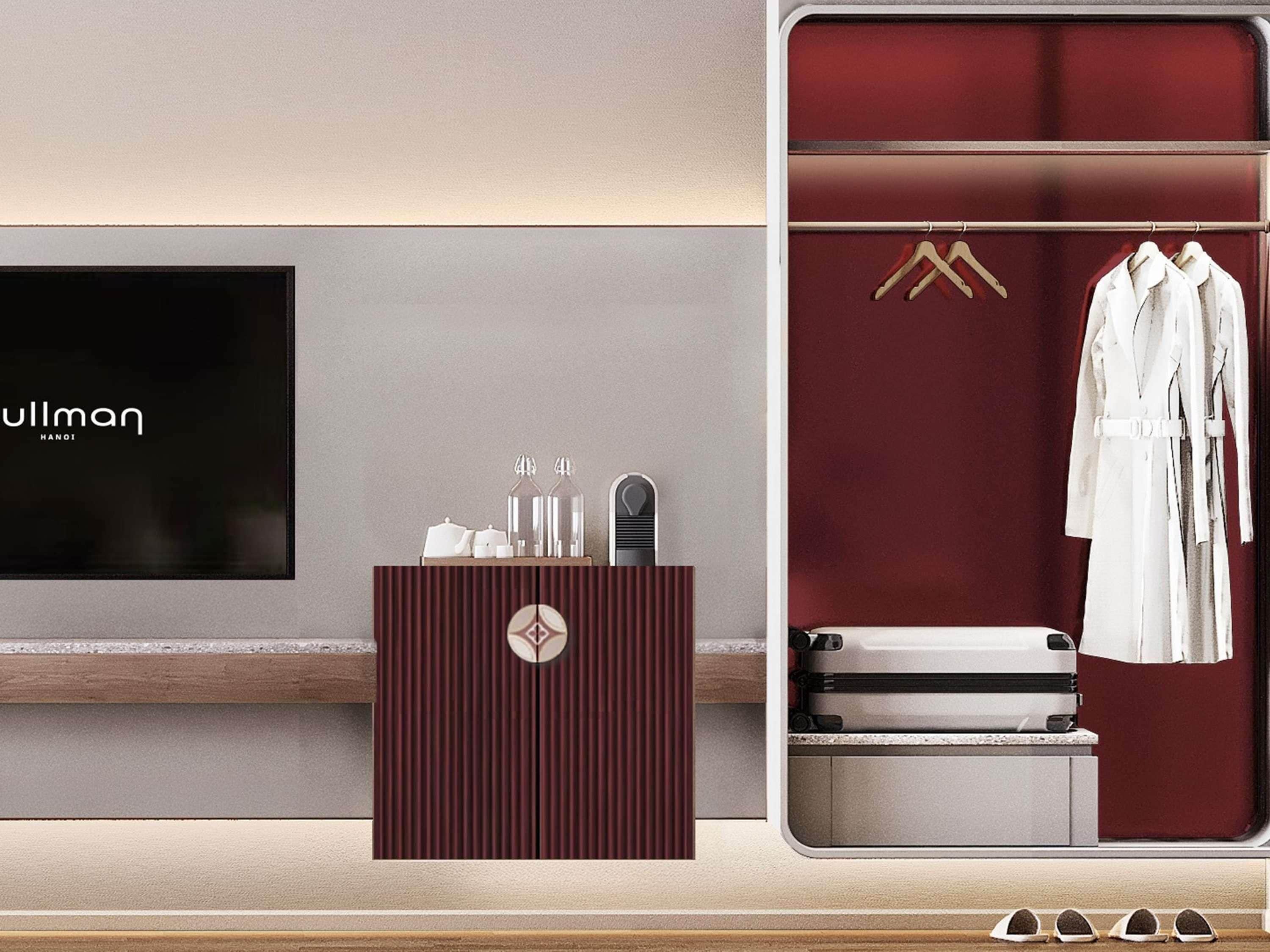 Habitación de hotel con minibar, espejo y perchero con batas blancas.