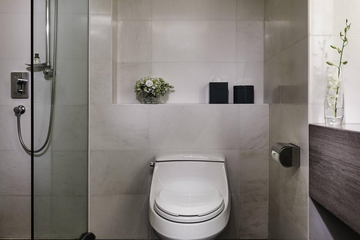 A modern bathroom with a glass-enclosed shower, a toilet, and a small shelf with a flower arrangement.