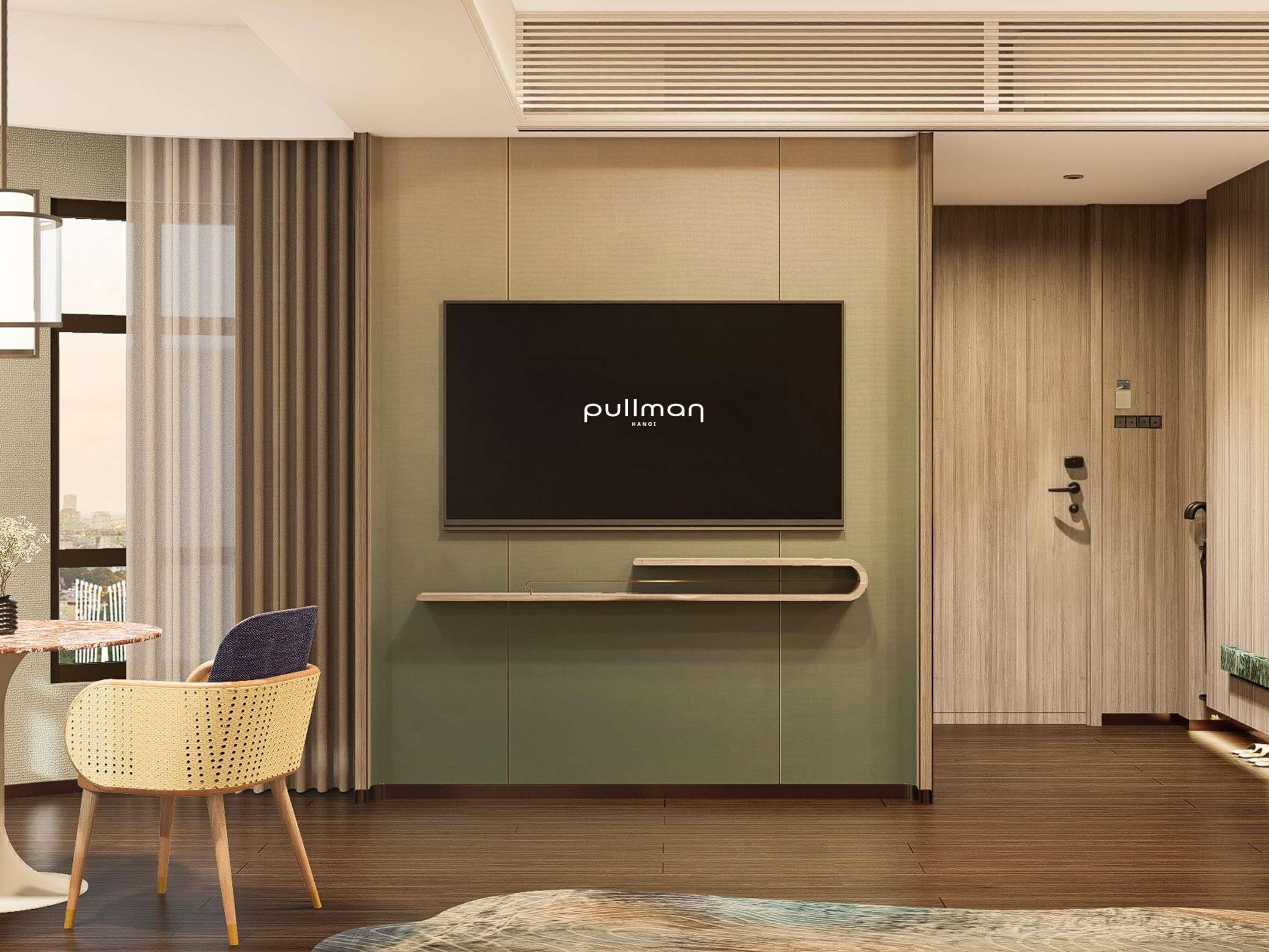 A modern hotel room with a flat-screen TV mounted on a wall, a wooden floor, a wicker chair, and a view of the city through large windows.