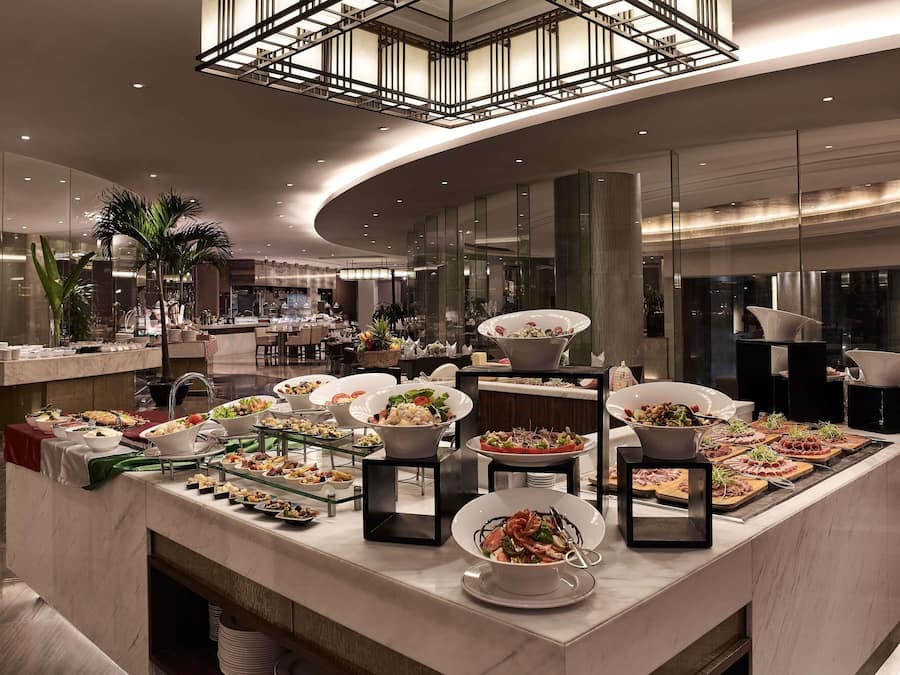 A modern hotel dining area with a variety of food options, a central serving station, and a contemporary interior design.