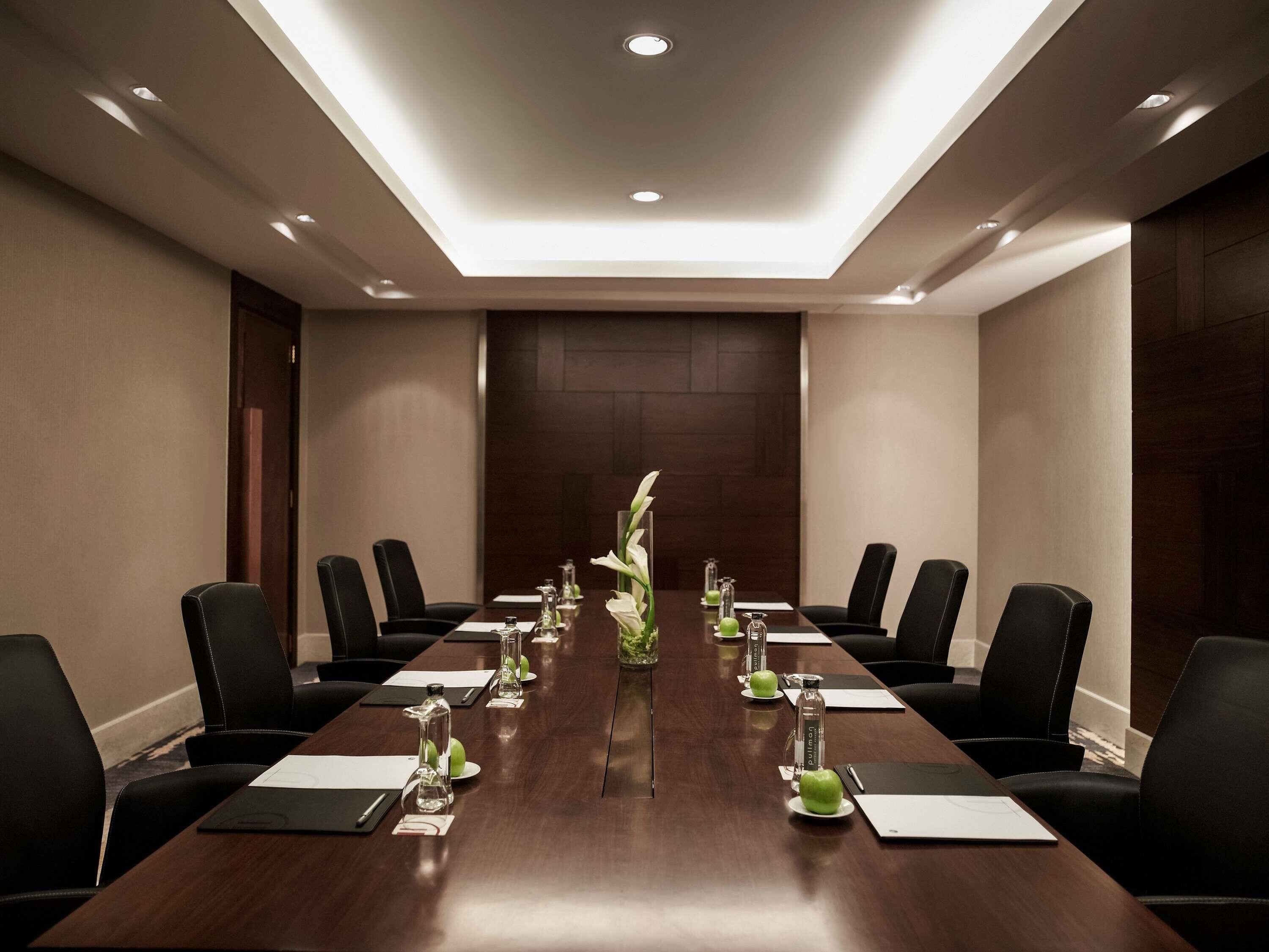 Un salón de conferencias con una larga mesa, sillas negras y una decoración central.