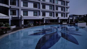 A modern hotel with a large pool featuring a geometric tile pattern, sun loungers, and umbrellas.