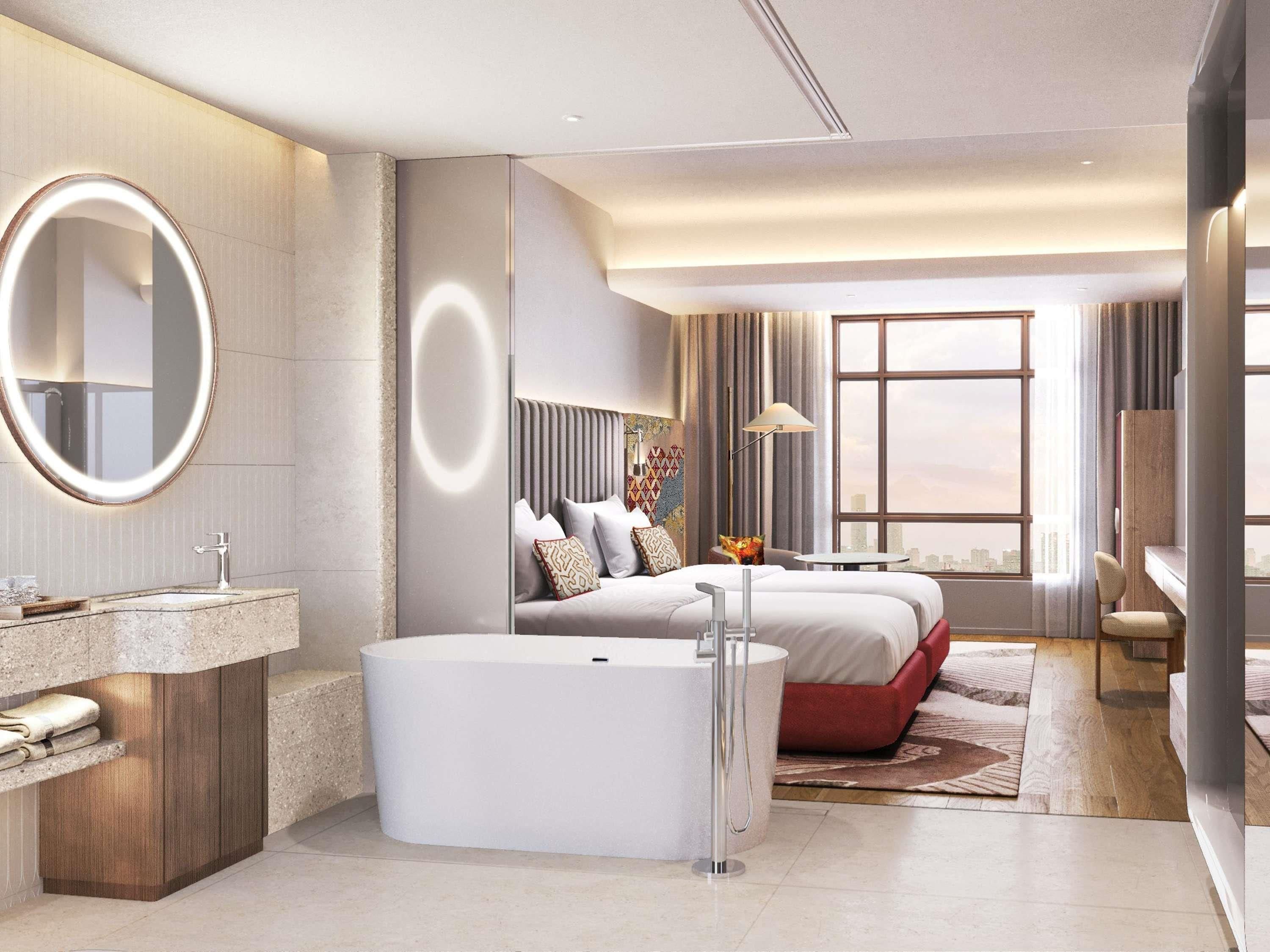 Een moderne hotelkamer met een groot bed, een eigen badkamer met badkuip, een ronde spiegel en uitzicht op de stad.