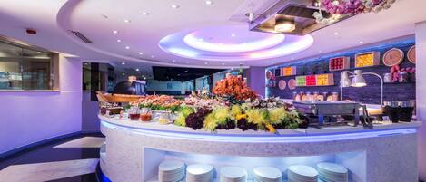 A modern hotel lobby with a central counter displaying a variety of food items and a decorative ceiling.