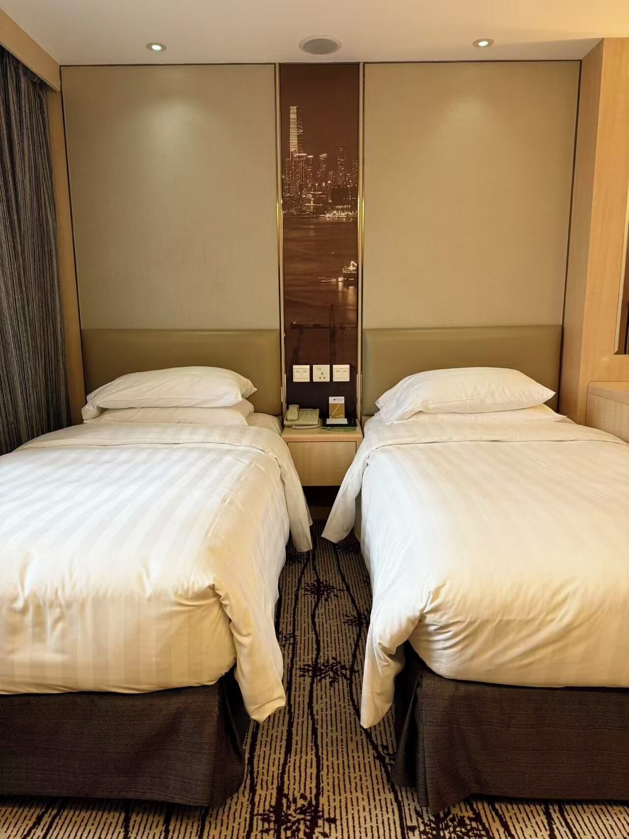A hotel room with two beds, a cityscape view, and a carpeted floor.