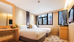 A hotel room with two beds, a desk, a mirror, a TV, and a view of the city through large windows. - Metropark Hotel Mongkok (Kowloon)