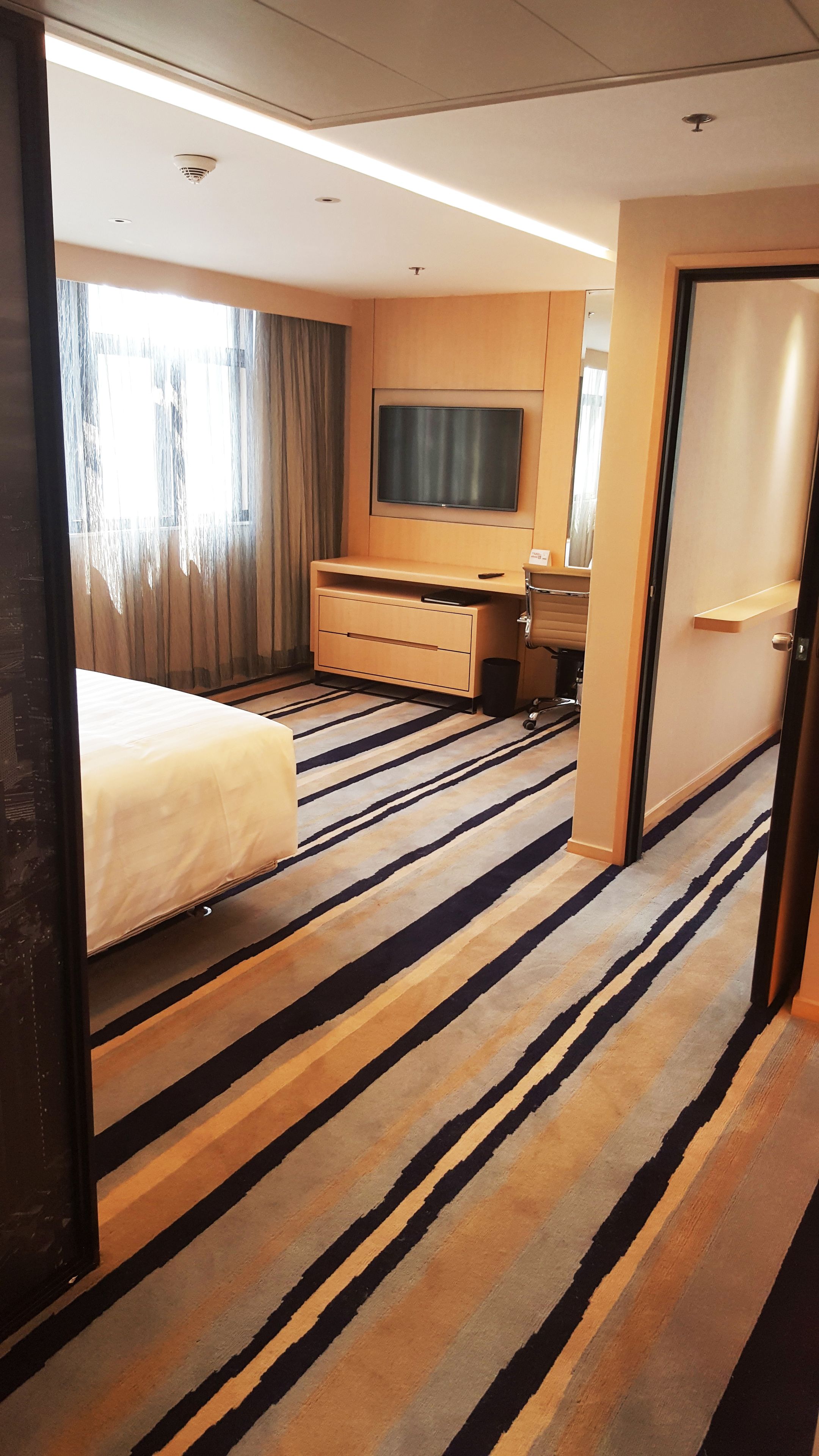 Una habitación de hotel con una cama, un televisor en la pared, un escritorio y una puerta.
