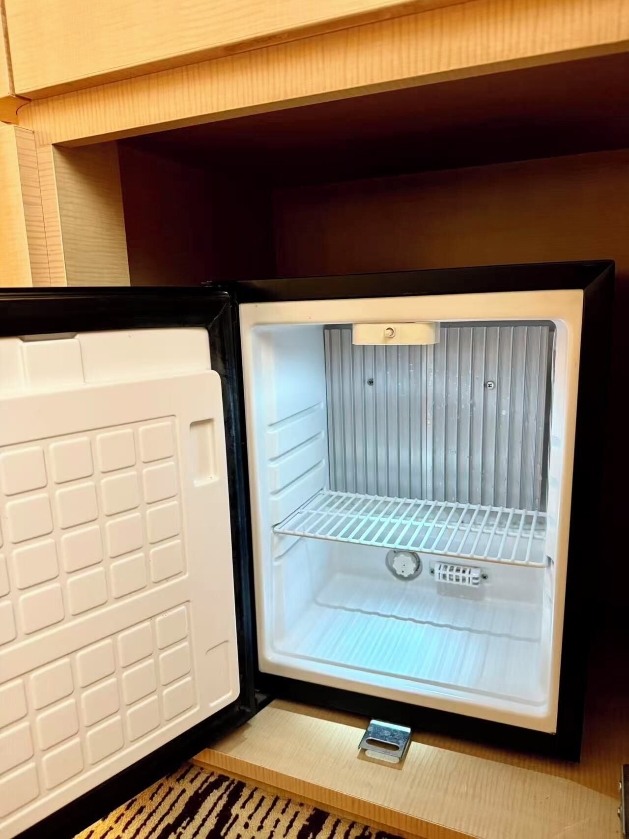 An open refrigerator with a metal shelf and a small ice maker.