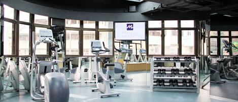 A gym with various exercise equipment, large windows, and a mirrored wall.