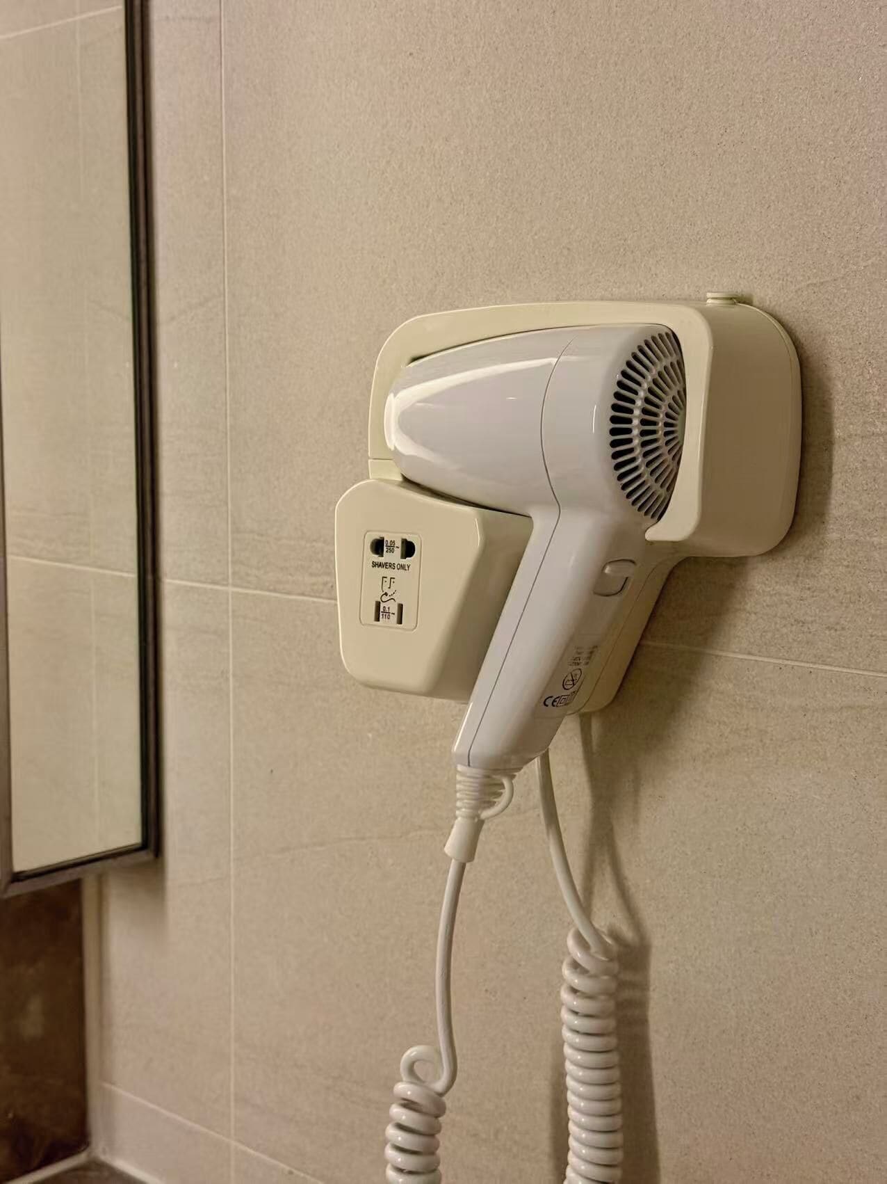 A hair dryer mounted on a wall with a coiled cord.