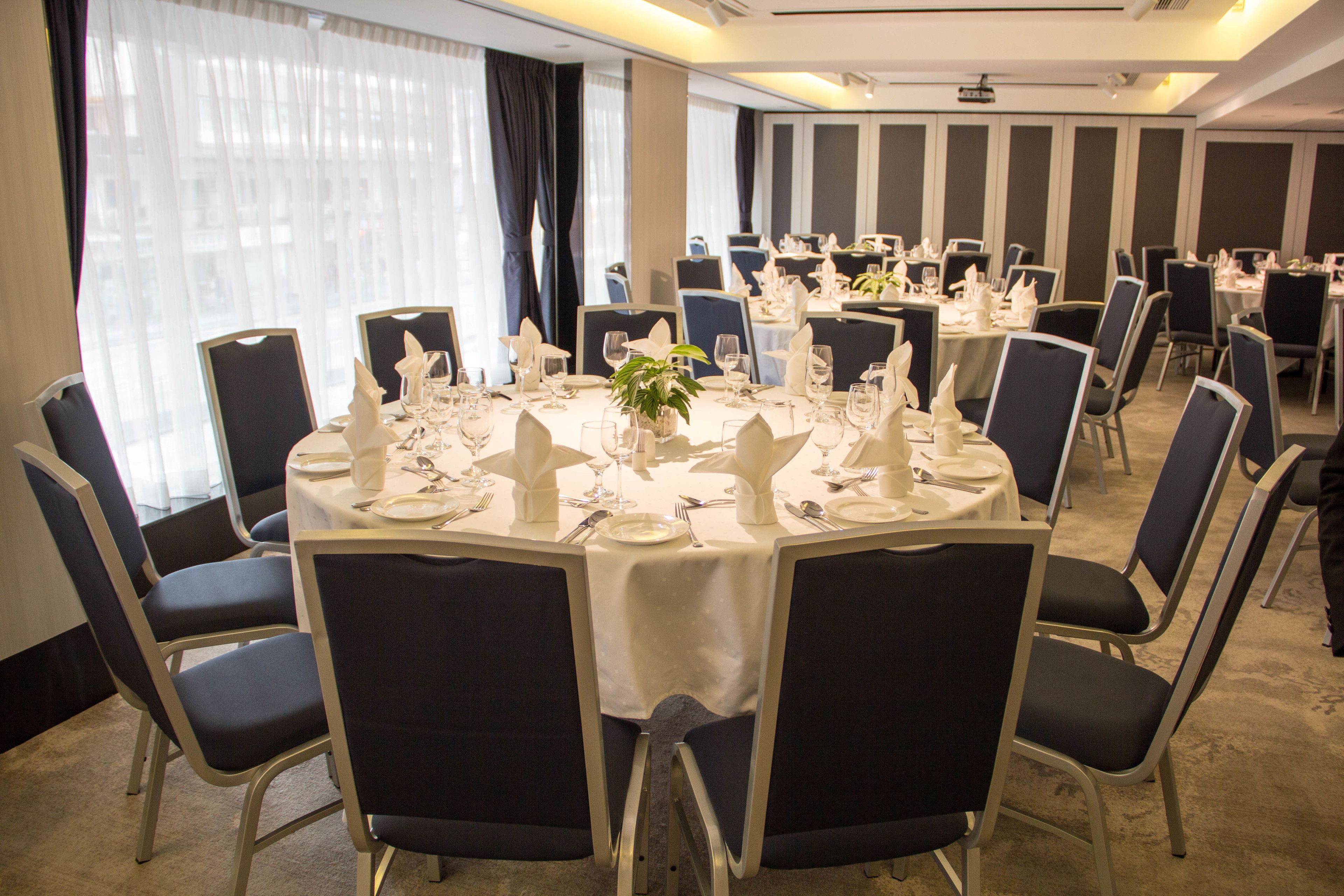 A conference room with round tables, black chairs, and white tablecloths.