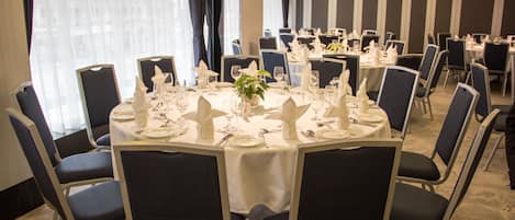 A conference room with round tables, black chairs, and white tablecloths.