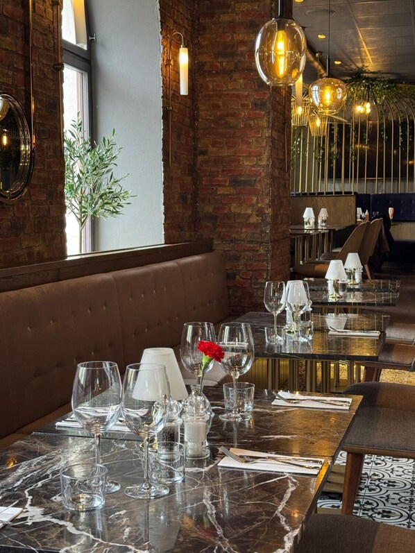 A restaurant with marble-topped tables, leather booths, and hanging pendant lights.