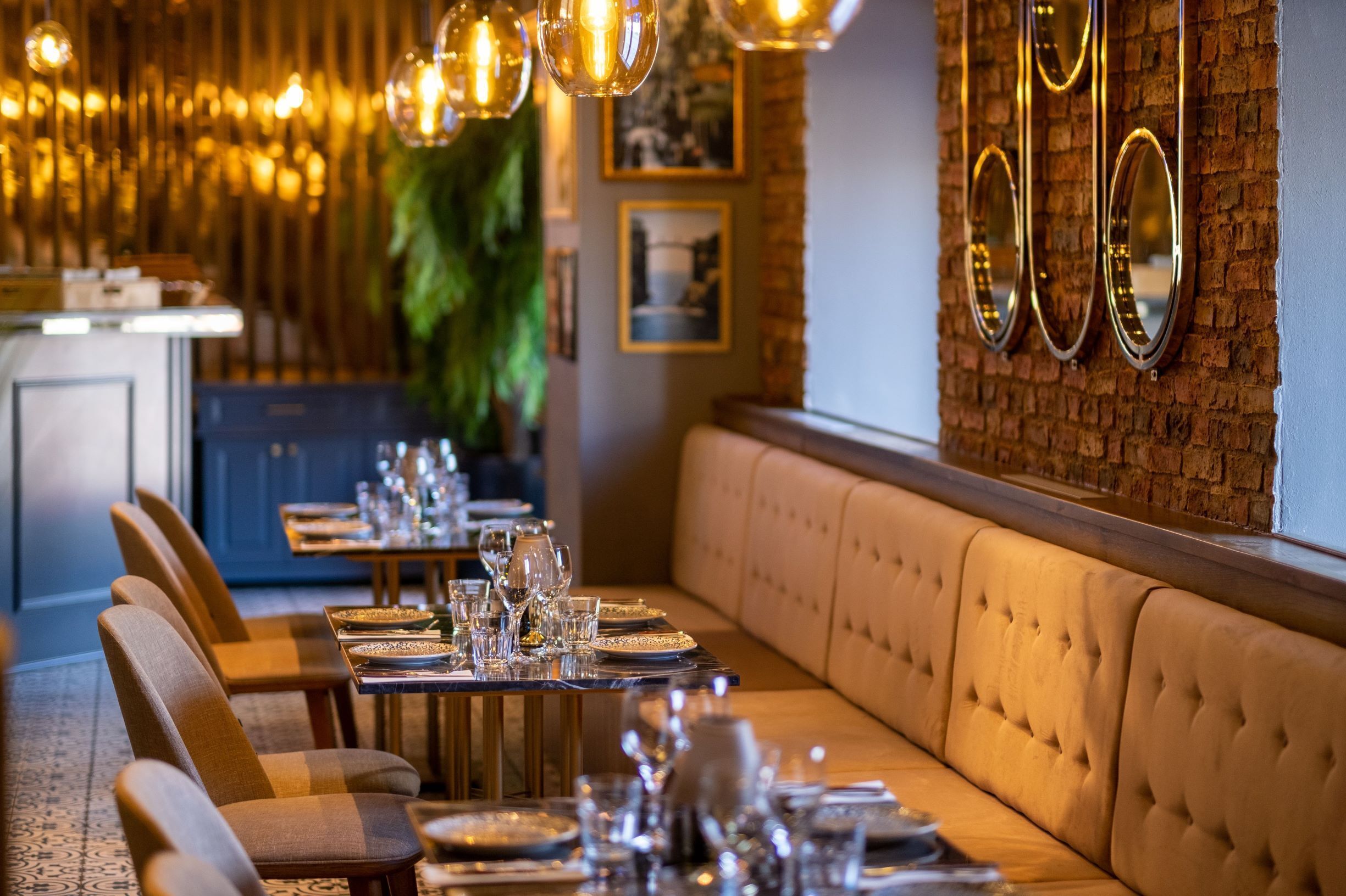 Un restaurante con una larga mesa de comedor dispuesta para una comida, un banco acolchado a lo largo de la pared y lámparas colgantes.