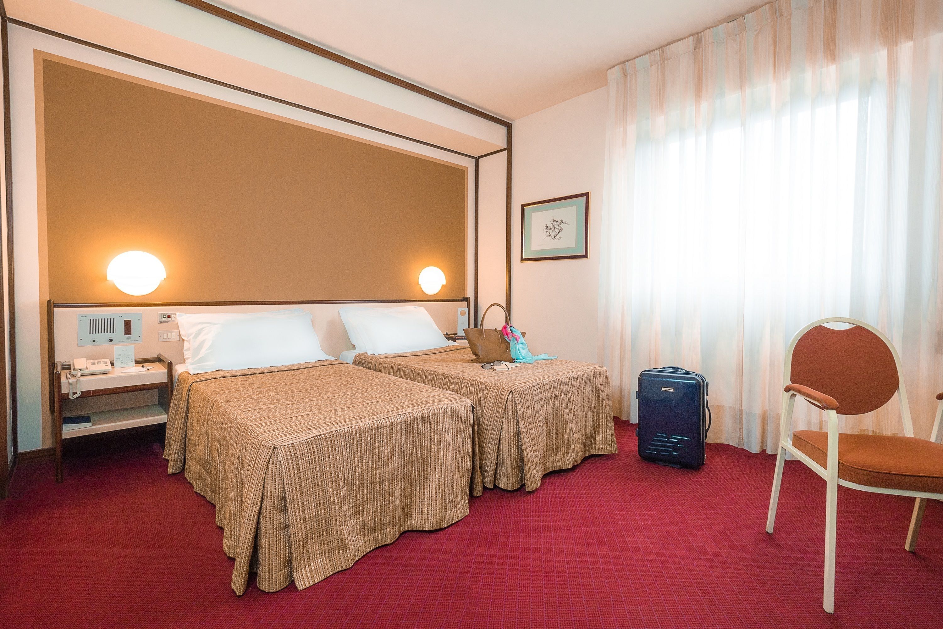 A hotel room with two beds, a desk, a chair, and a suitcase.
