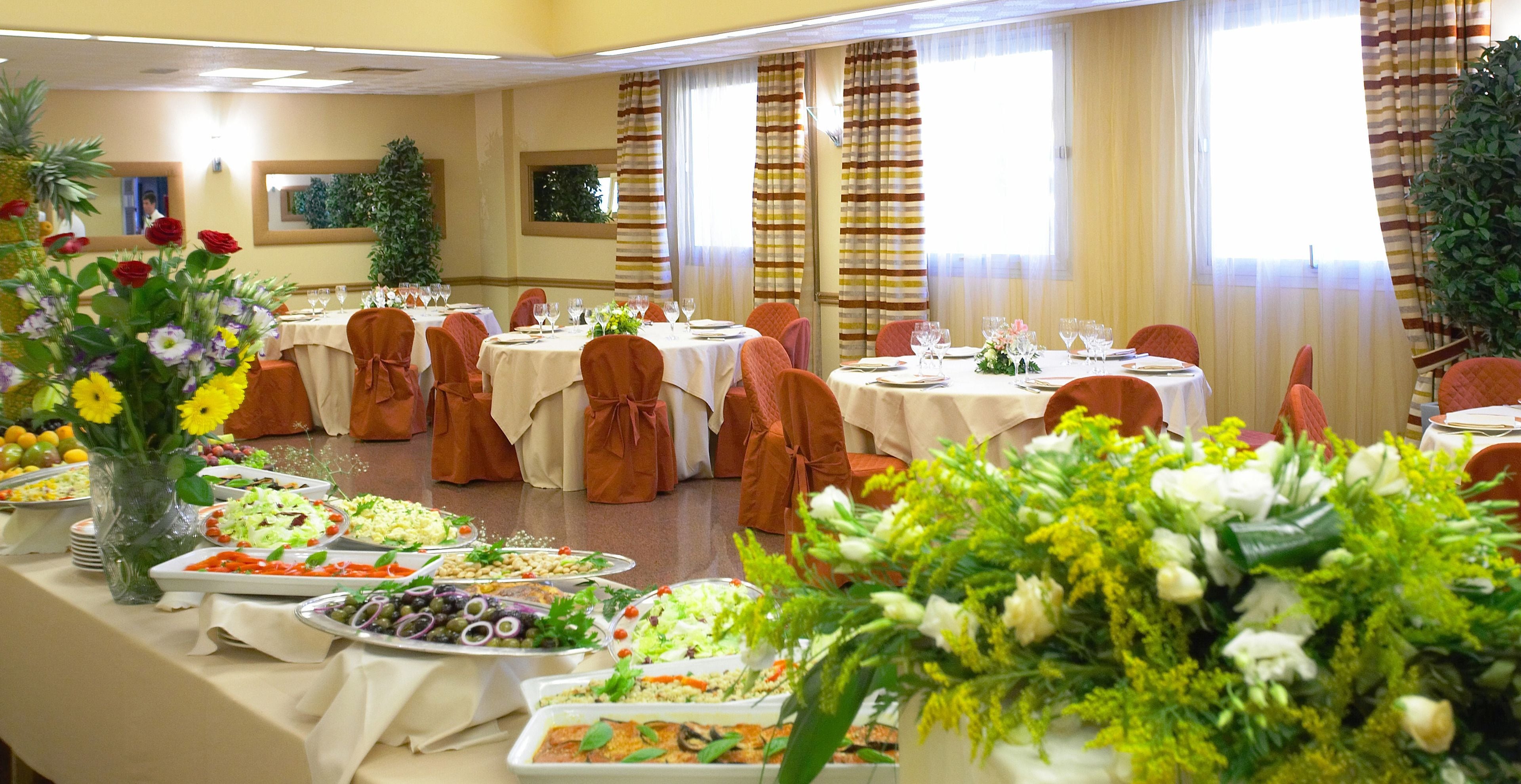 Une salle de banquet avec des tables rondes, des chaises et un buffet proposant divers plats.