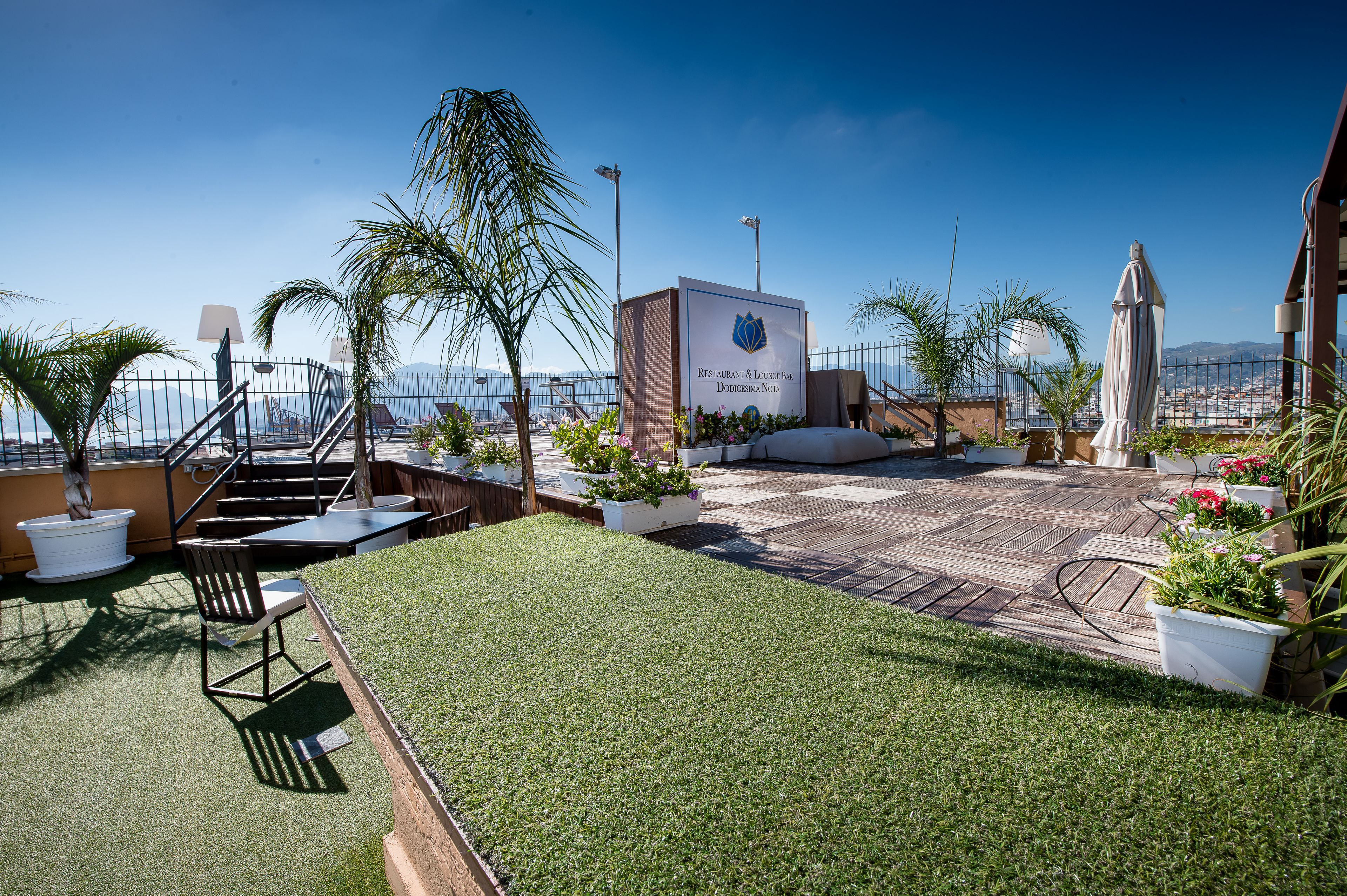 A rooftop terrace with a sign for a restaurant and lounge bar, outdoor seating, and a view of the city.