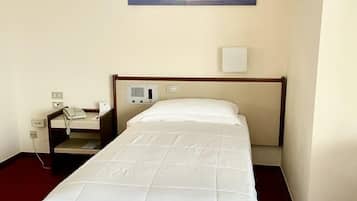 Una habitación de hotel con una cama, una mesita de noche, un teléfono, un cuadro de un barco en el agua y una alfombra roja.