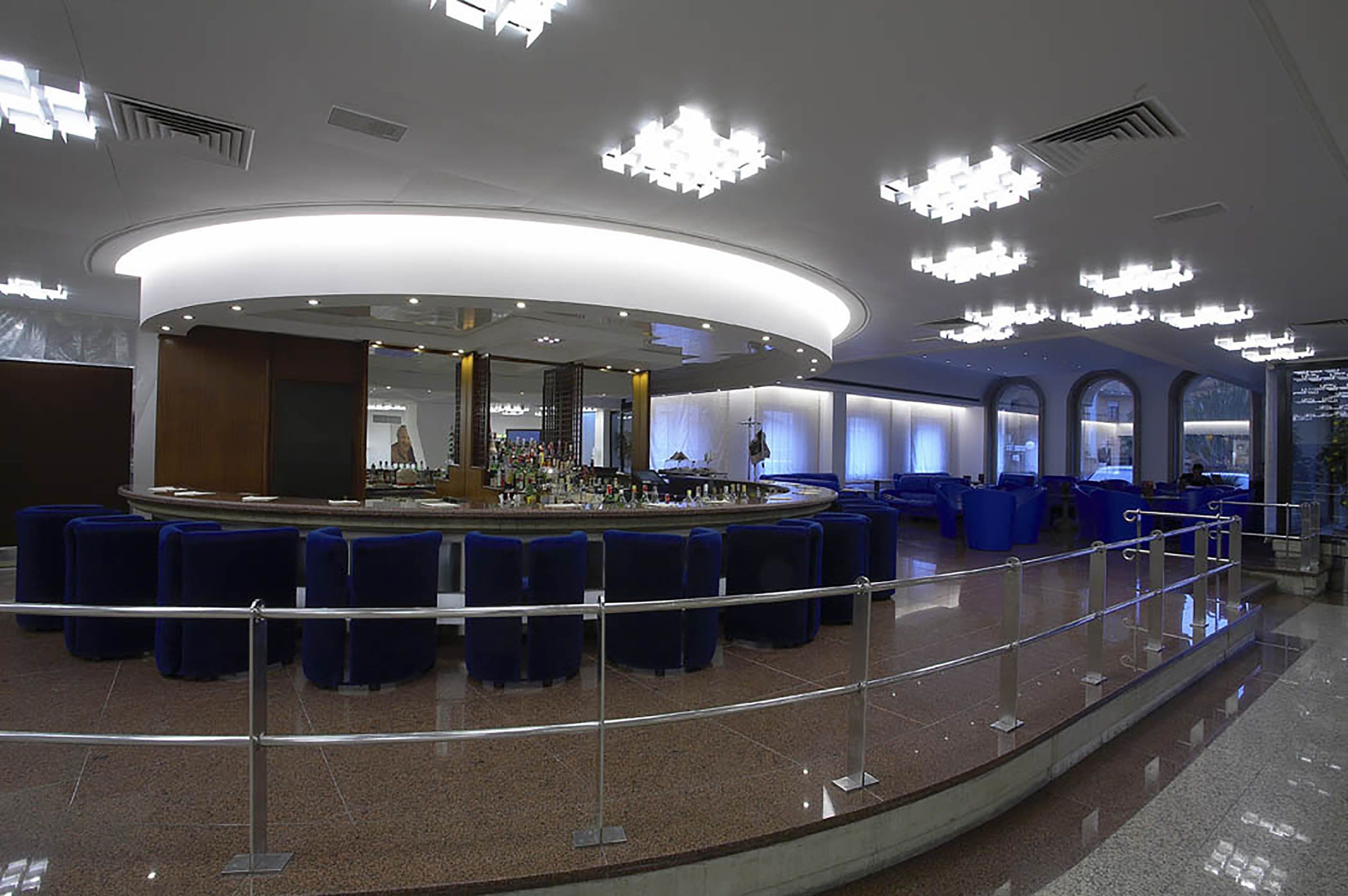 A modern lobby with a central bar area, seating arrangements, and a glass railing.