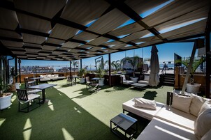 Une terrasse sur le toit avec des espaces de détente en plein air, comprenant des canapés et des tables, ainsi que des plantes en pot.