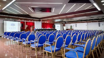 A conference room with rows of blue chairs, a podium, and a screen displaying 'GHS'.