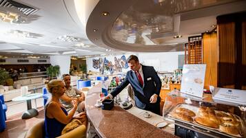 Eine moderne Hotelhalle mit gewölbter Decke, Sitzbereichen und einer Theke mit Kaffeeangebot.