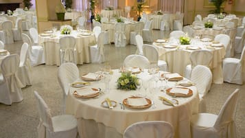 Une salle de banquet avec des tables rondes dressées pour un événement formel, chacune étant recouverte d’une nappe blanche et agrémentée de chaises et de compositions florales.