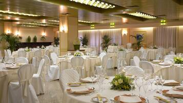 Un salón de banquetes con mesas redondas dispuestas para comer, sillas blancas y centros de mesa florales.