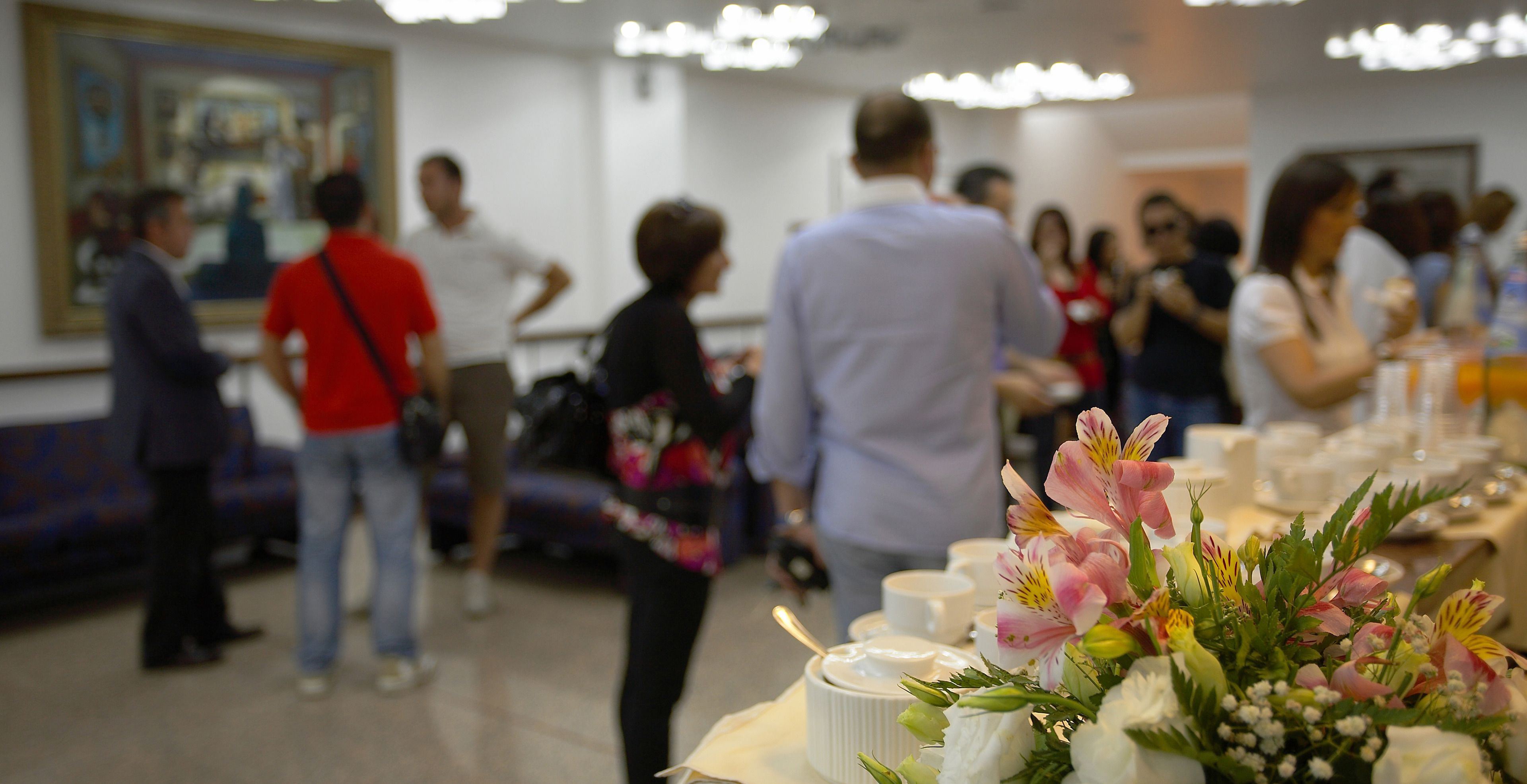 Un groupe de personnes se trouve dans un espace intérieur bien éclairé, autour d’une table dressée pour un repas, agrémentée d’un arrangement floral.