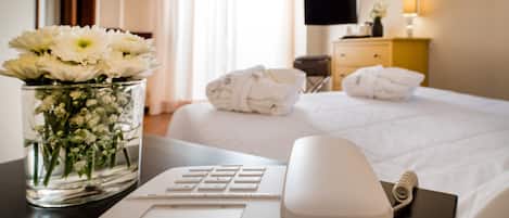 Una habitación de hotel con una cama, un escritorio con computadora, un jarrón de flores y un televisor en la pared.