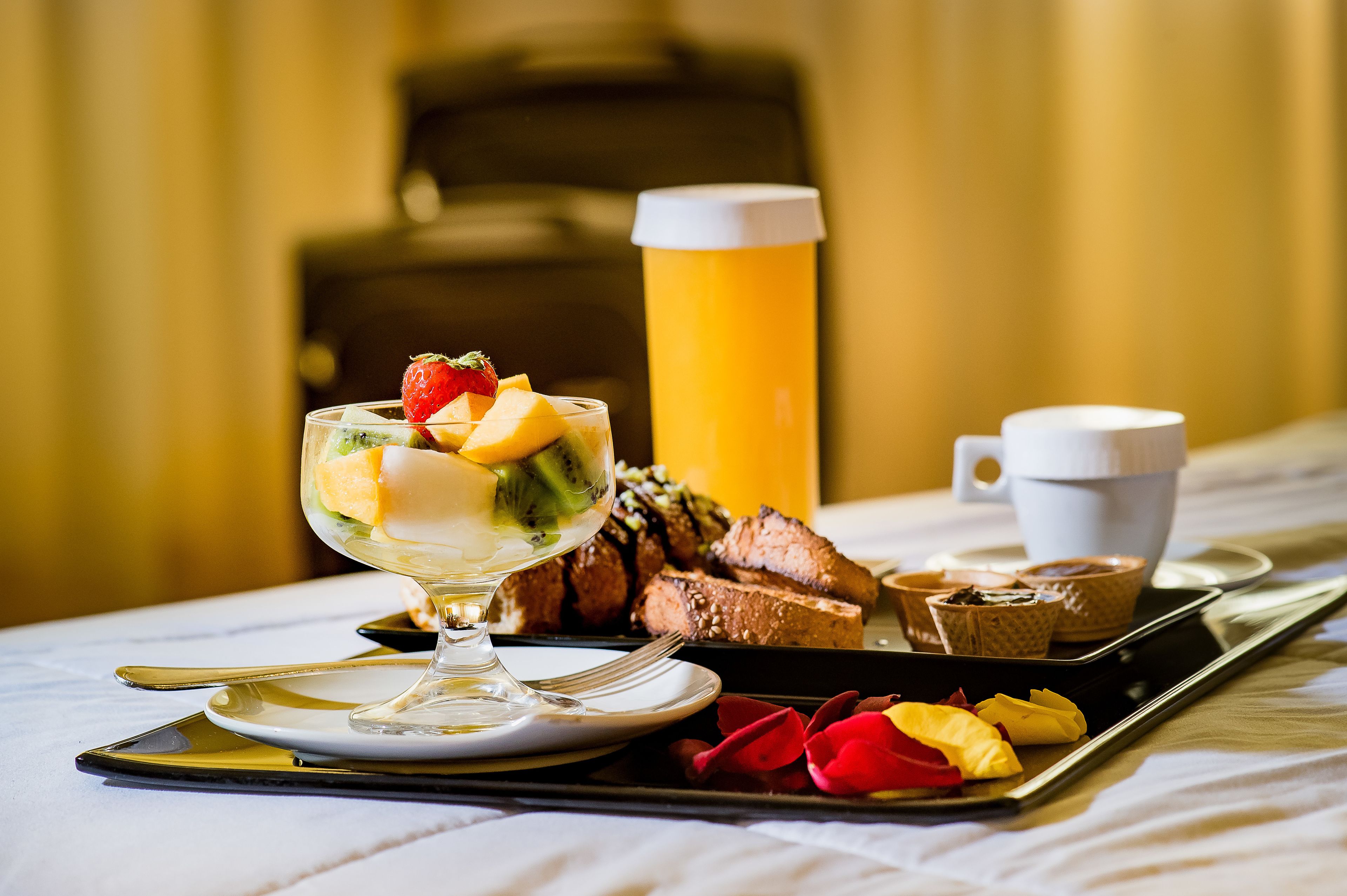 A breakfast tray with a dessert, coffee, and pastries on a hotel bed.