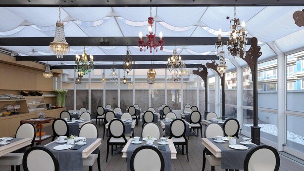 Un restaurant doté de nombreuses tables et chaises, de lustres et offrant une vue sur l’extérieur grâce à de grandes fenêtres.