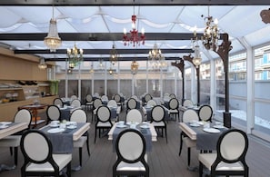 A restaurant with multiple tables and chairs, chandeliers, and a view through large windows.