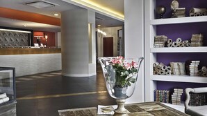 Un espace d’accueil au design moderne, comprenant un comptoir de réception, un grand vase rempli de fleurs et une bibliothèque contenant divers objets.