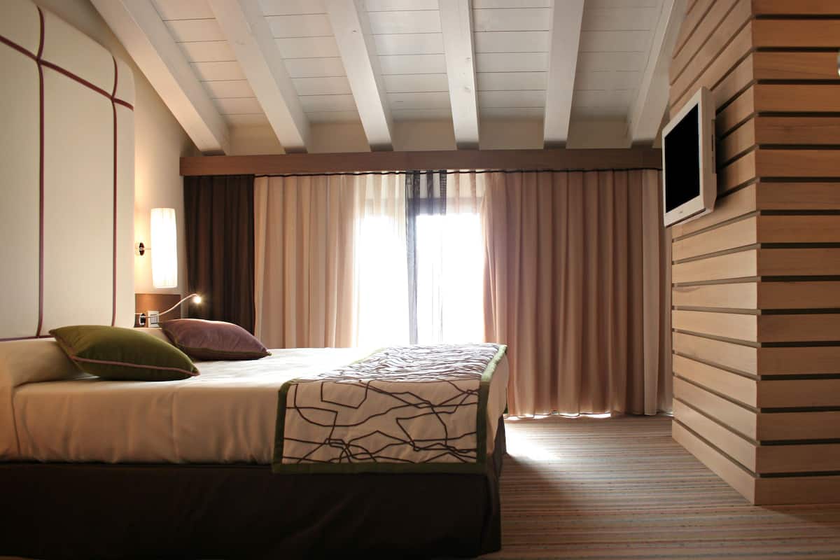 A hotel room with a bed, a bedside lamp, a TV mounted on the wall, and a window with curtains.