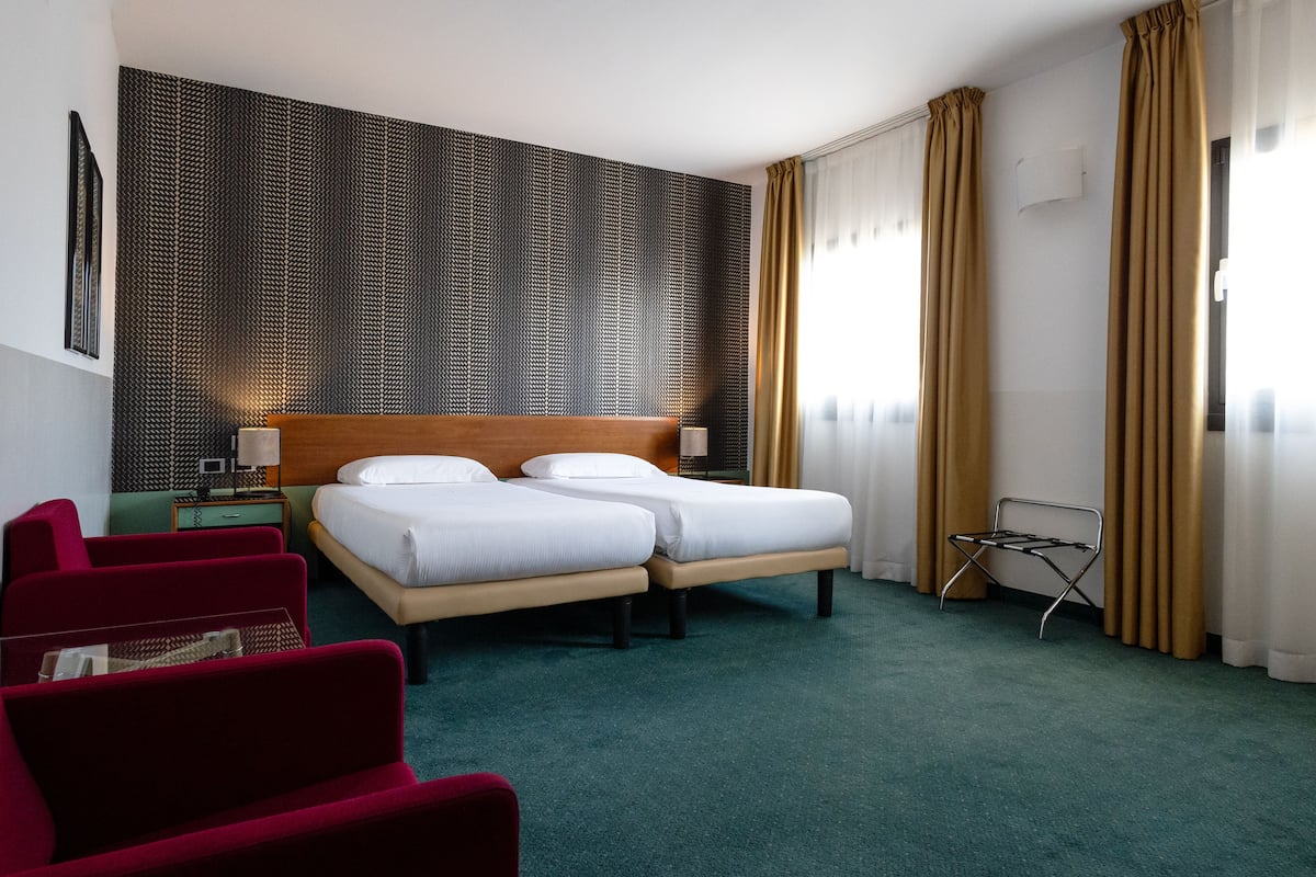 A hotel room with a large bed, two bedside tables, a red chair, and a patterned wall.