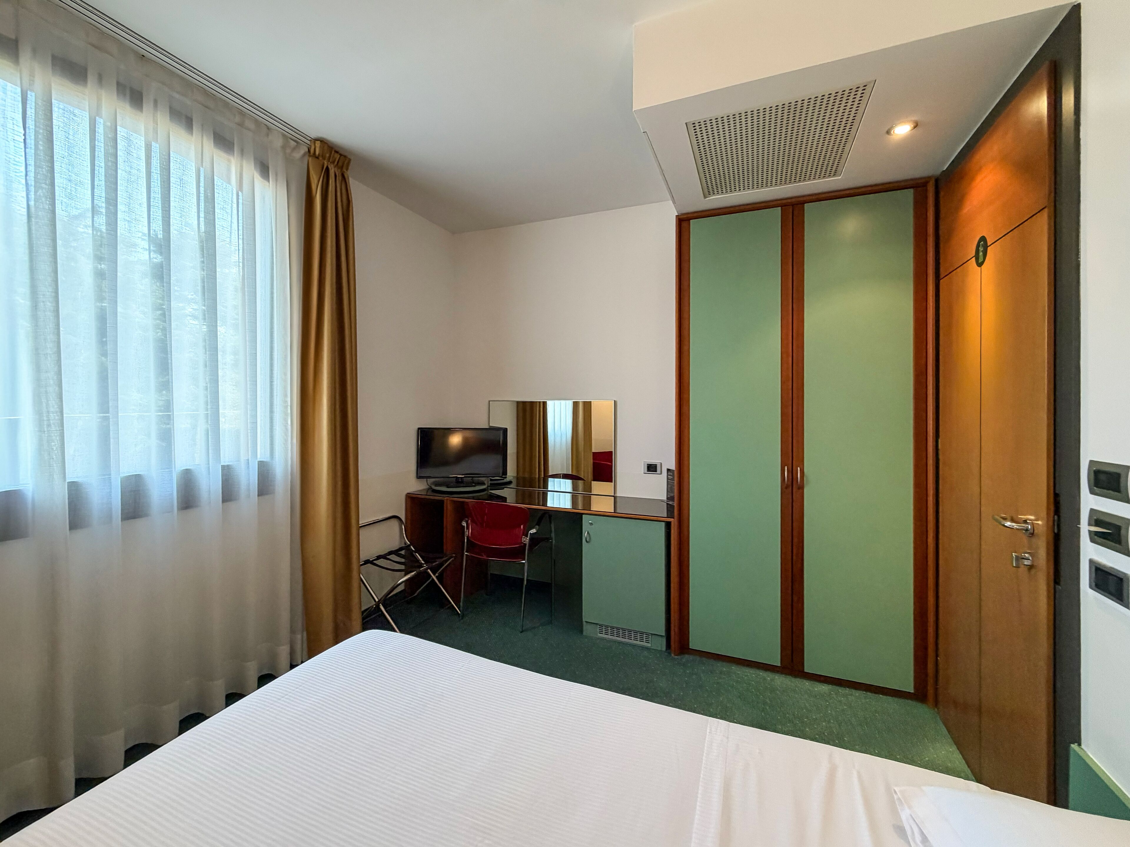 Ein Hotelzimmer mit einem Bett, einem Schreibtisch mit Stuhl, einem Fernseher und einem Kleiderschrank.