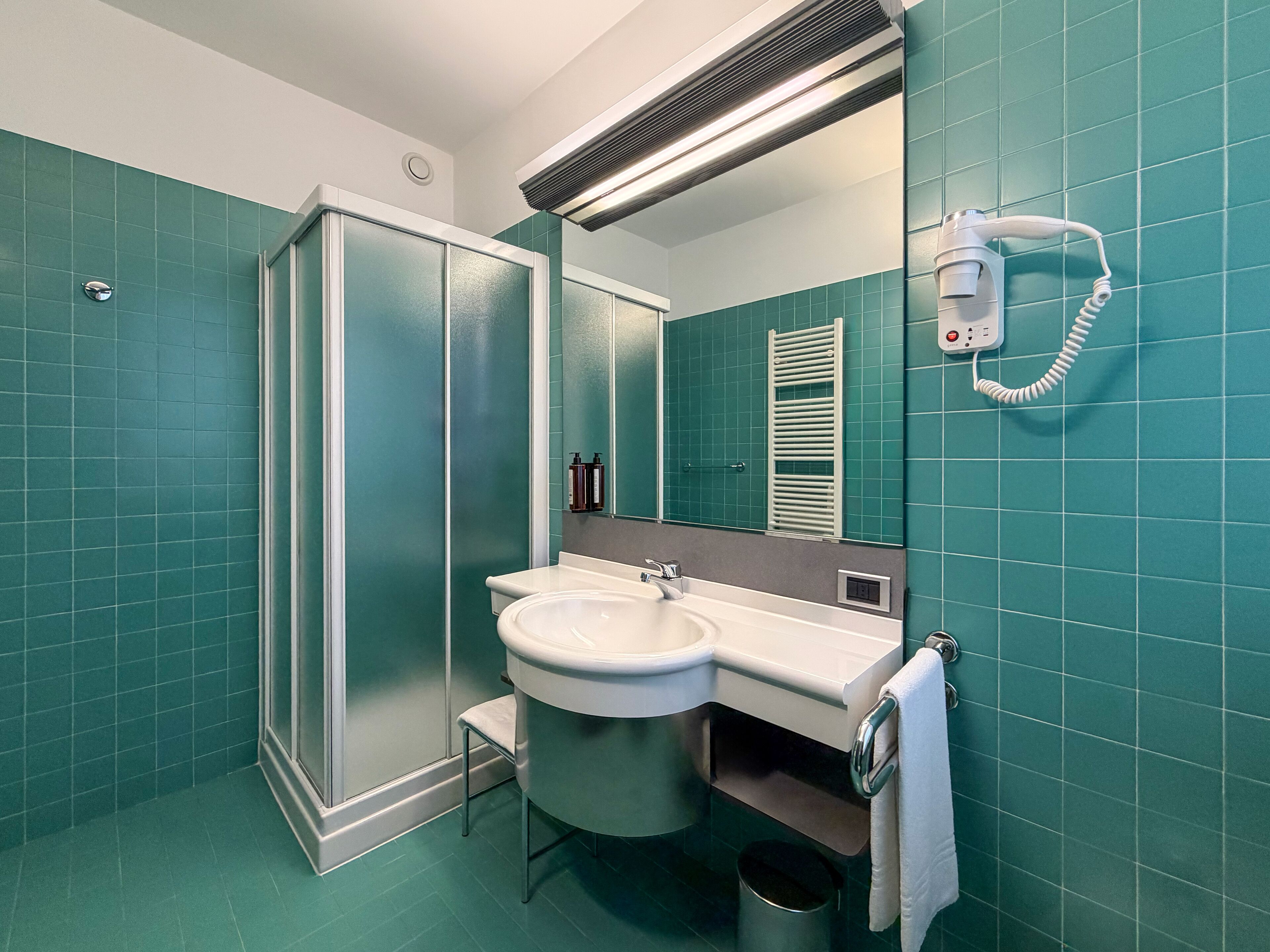 A bathroom with a shower, sink, and hairdryer.