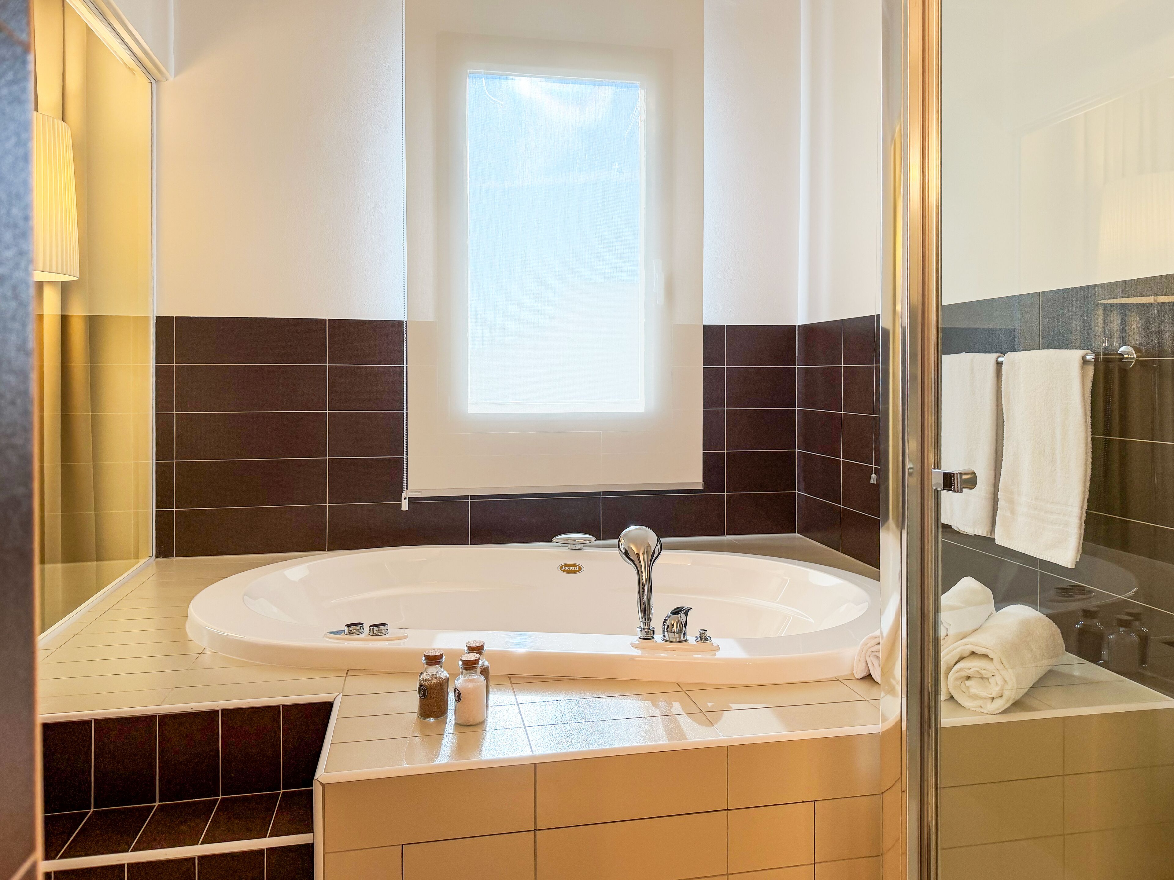 A modern bathroom with a freestanding bathtub, a large mirror, and a window providing natural light.