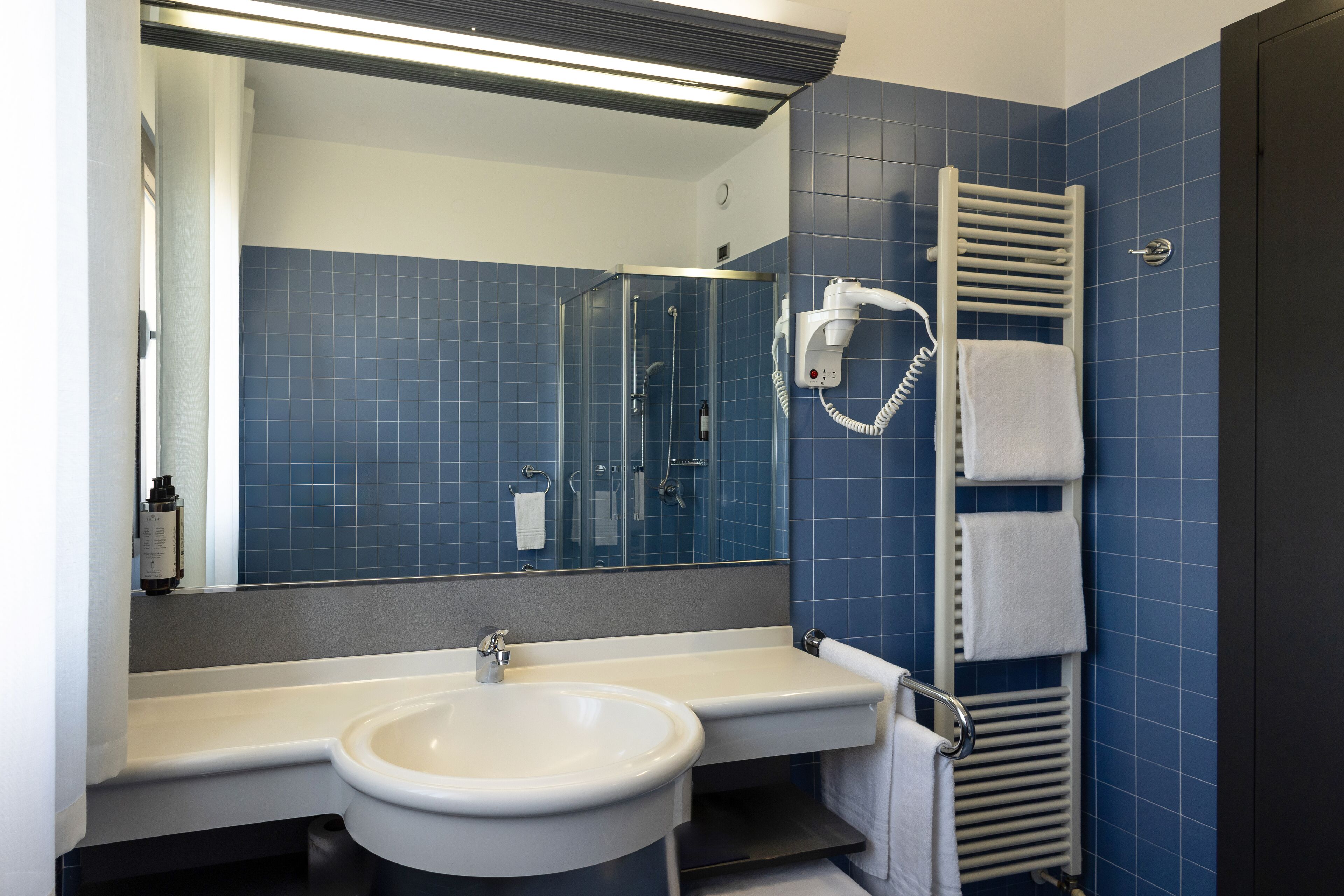 A bathroom with a sink, mirror, shower, and towel rack.