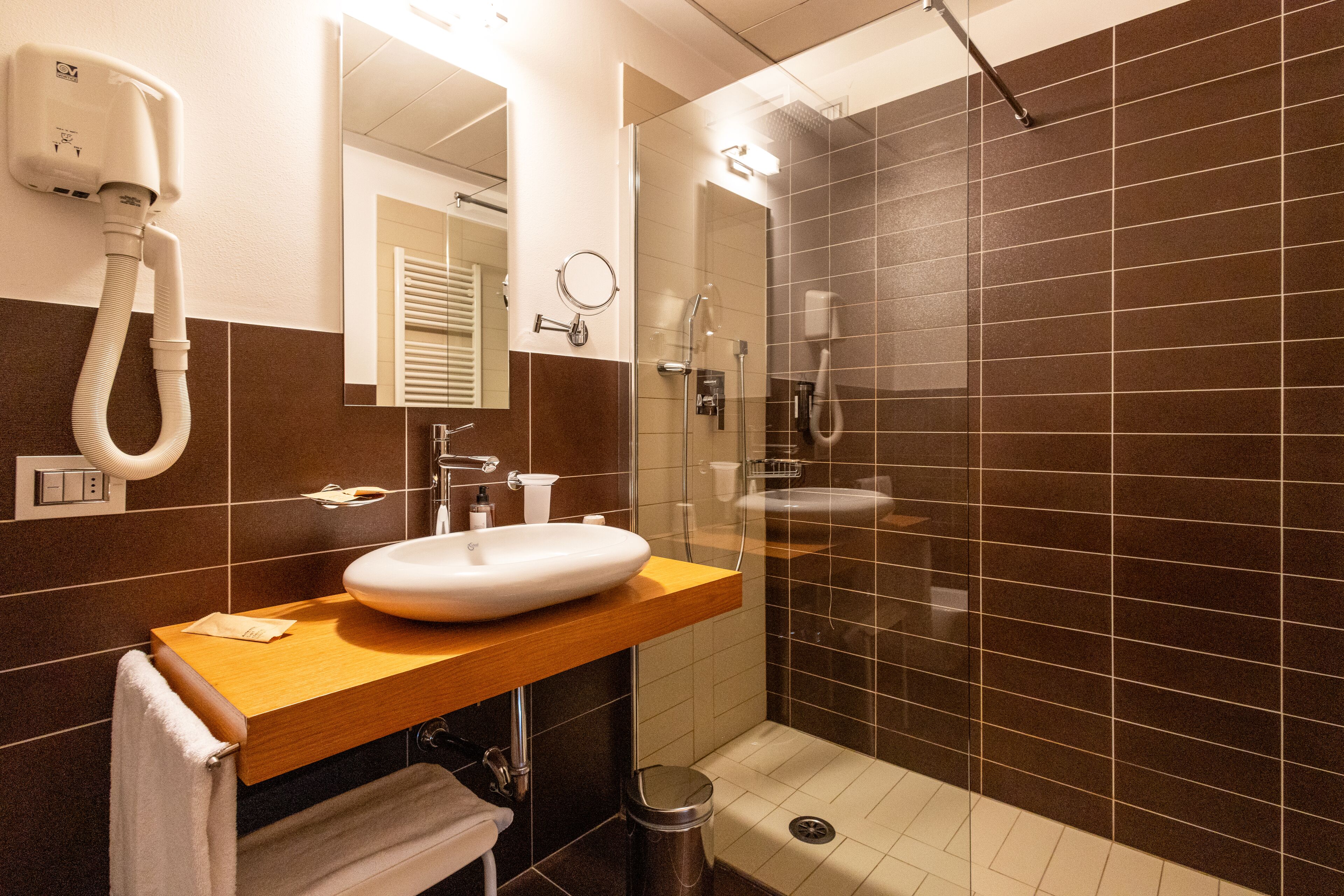 A modern bathroom with a wooden vanity, a white sink, a glass shower enclosure, and a towel rack.