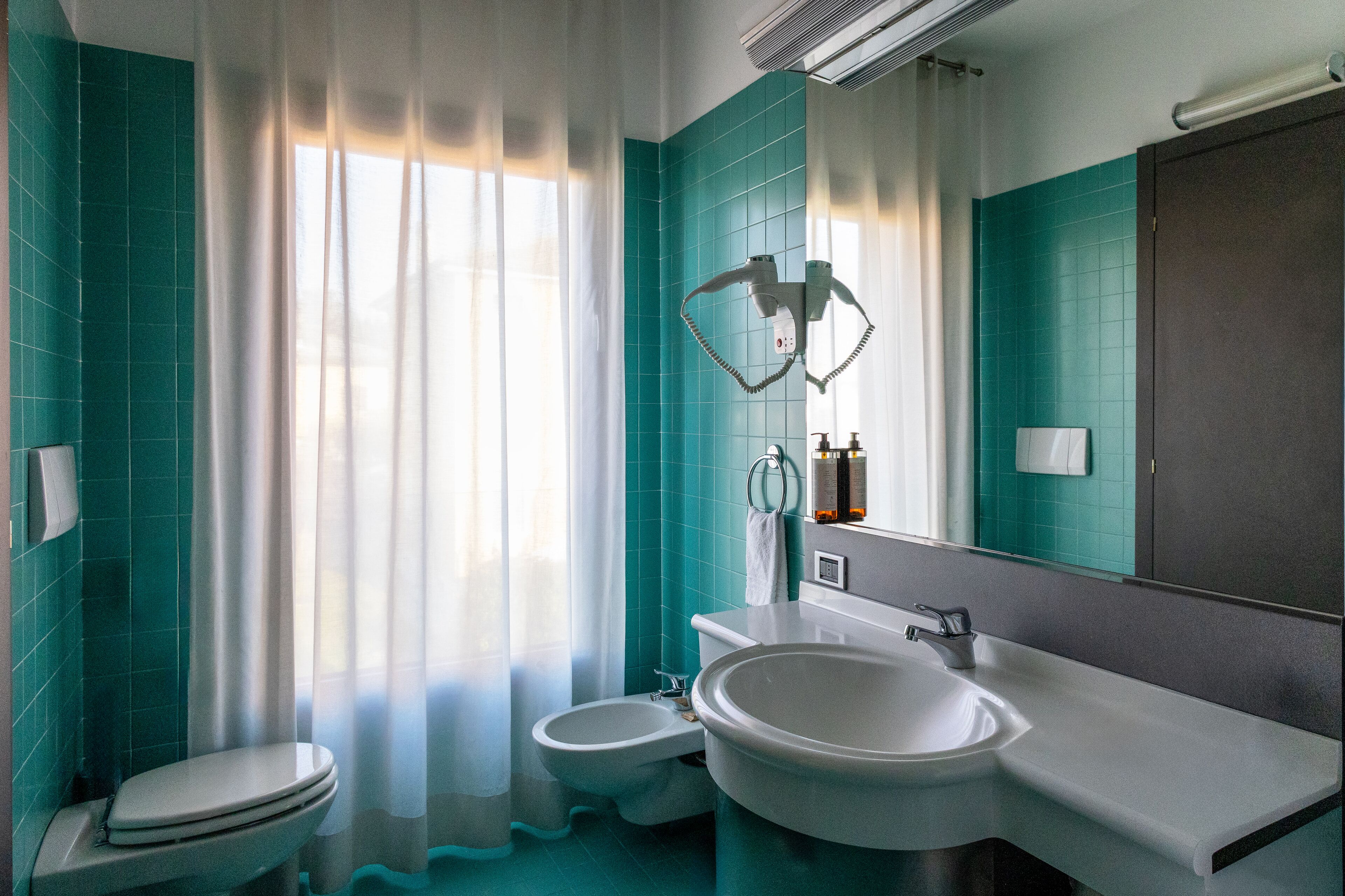 Ein Badezimmer mit Toilette, Bidet und einem großen Waschbecken mit Spiegel darüber.