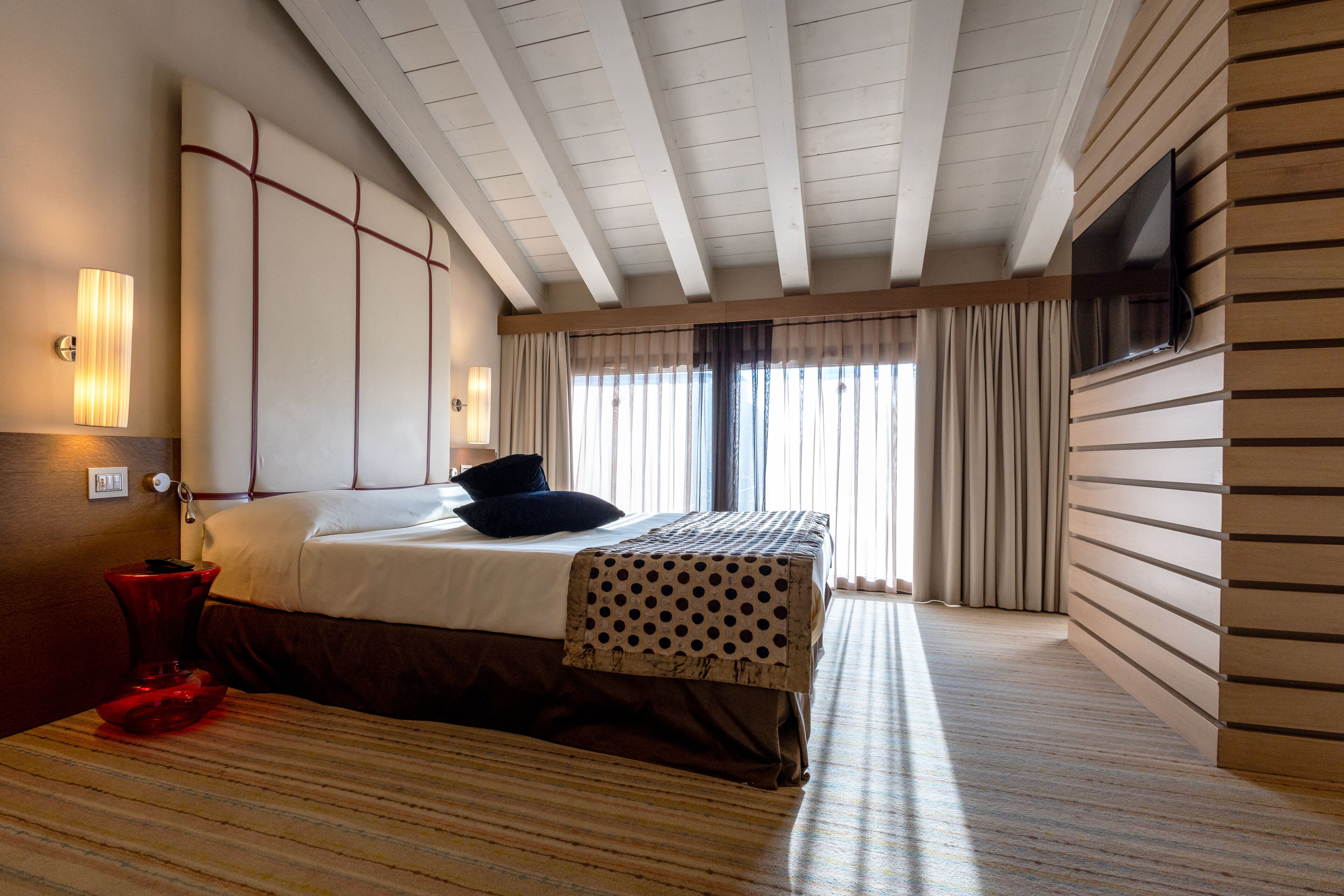 Une chambre d’hôtel avec un lit, un téléviseur fixé au mur et une fenêtre avec des rideaux.
