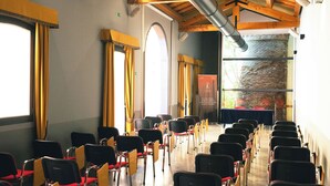 A conference room with rows of chairs, a stage with a table, and a brick wall. - Hotel Filanda (Cittadella)