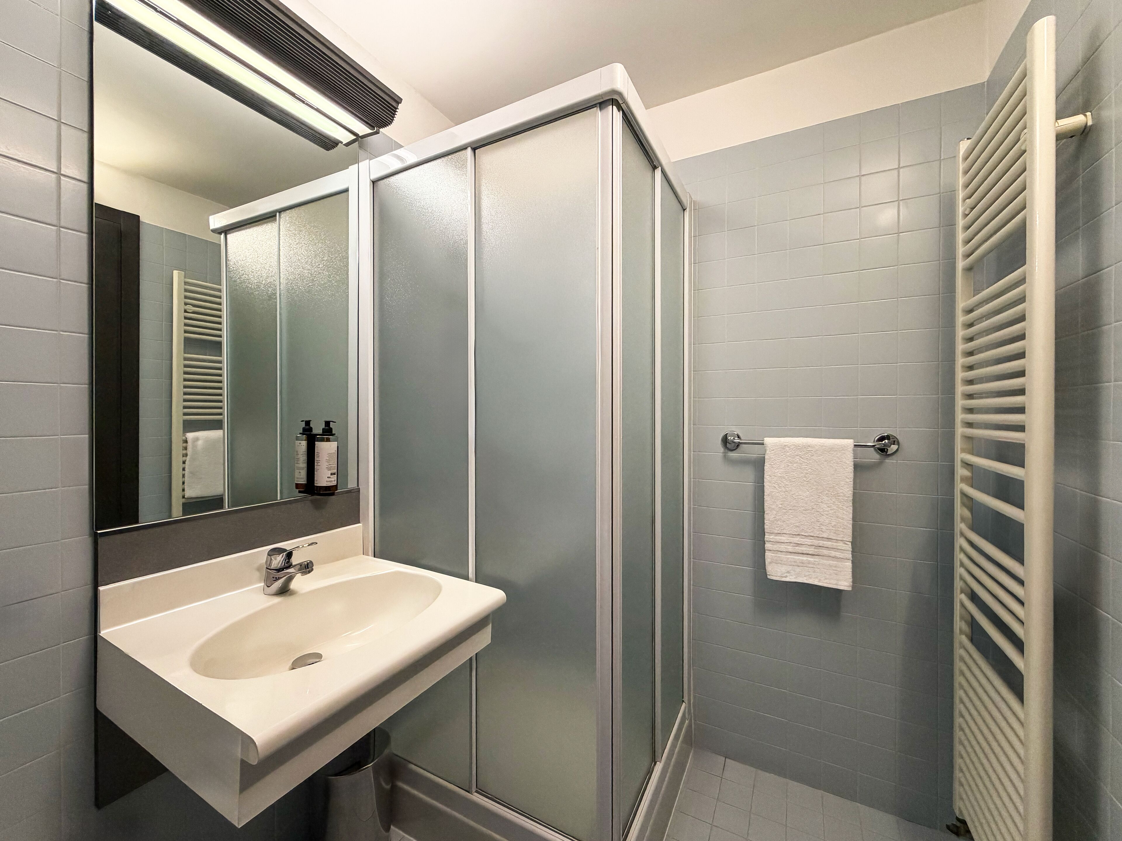 Un baño moderno con cabina de ducha de vidrio, un lavabo blanco y un perchero para toallas.