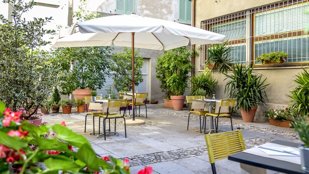 An outdoor patio with tables and chairs, surrounded by potted plants and a large umbrella. - Albergo Ristorante Tre Re (Como)